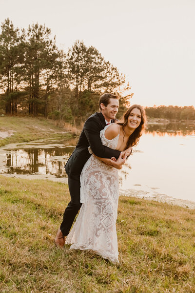 Newly wedded couple sharing a playful and joyful moment by the lake during their elopement in Spring, Texas, with the groom playfully lifting the bride as they laugh together.