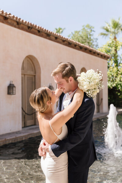 Bride holding classic white bouquet hugging groom and smiling at the Royal Palms Resort wedding venue in Scottsdale, Arizona.