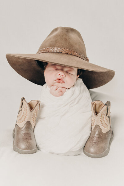 posed newborn baby wearing a cowboy hat with cowboy boots next to him - Townsville Newborn Photography by Jamie Simmons