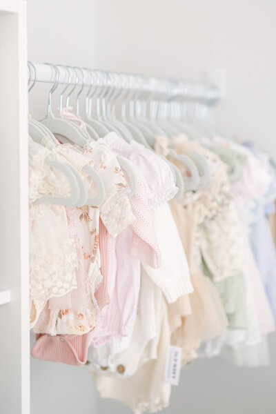 Photo of beautiful newborn baby outfits hanging on grey hangers in a line in a bright louisville kentucky studio taken by louisville newborn photographer missy marshall photography
