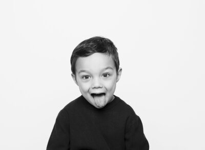 Young boy in black and white portrait sticking his tongue out