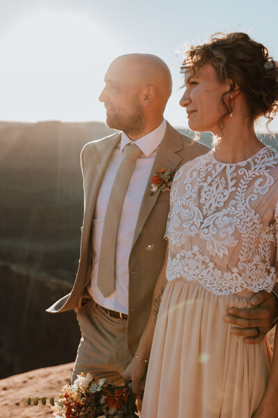 groom standing with his arm around his bride's waist while they both look off into the distance