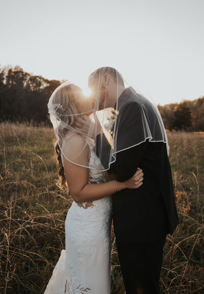 outdoor wedding in Knoxville with bride and groom kissing as the sun sets in the distance through the trees photographed by Knoxville wedding photographers