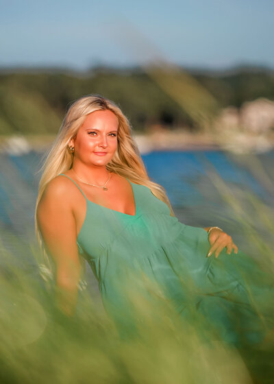 High school senior girl sitting on the beach with grass in front of her while posing for a South Shore, MA portrait photographer.