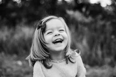 A joyful young girl smiling broadly in a black and white outdoor setting, captured by a skilled family photographer in Pittsburgh, PA.