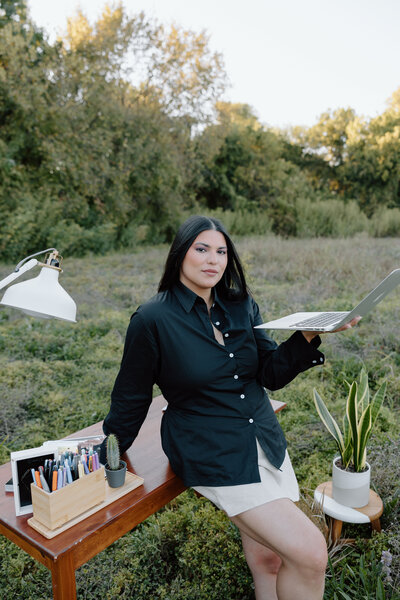 Veronica, the owner of Vemi Studio leaning on the desk holding her laptop
