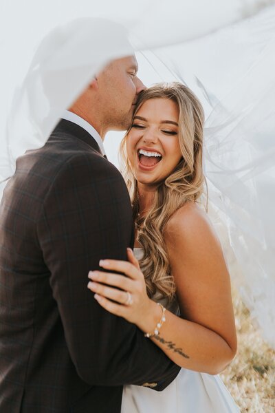 a Colorado wedding photography couple laughing under a wedding veil
