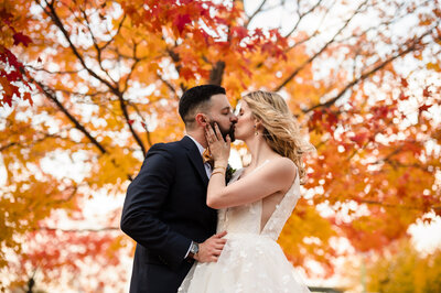Bride and groom kiss in front of a fall colored tree