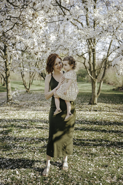 Verona B Photography captures a picture of a mom holding her young daughter surrounded by flowering trees at Nature Realm in Akron.