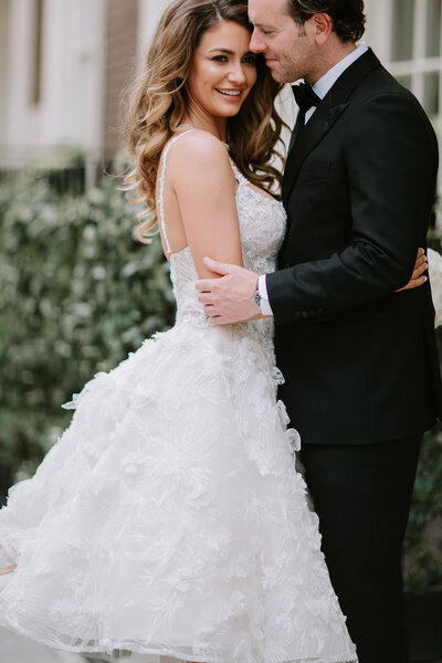 Image of a bride and groom at The Arts Club in Mayfair, London. The bride wears a beautiful lace gown and smiles while embracing the groom in a black tuxedo.