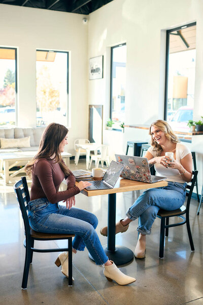 two girls sitting at a coffee shop table working on computers