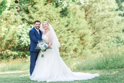 Bride and groom in green field blue white and blush flowers