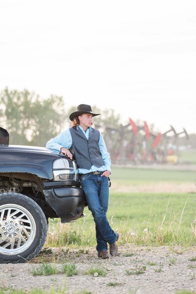 picture of grad leaning on a black truck with pump jacks in the background