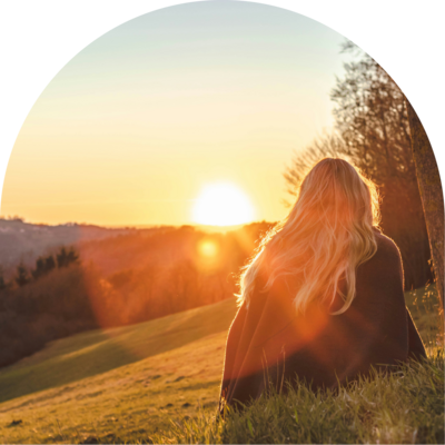 woman sits on grass watching sunset