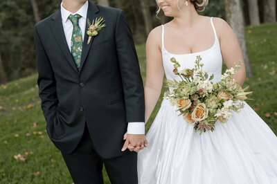 A photo of a bride and groom holding hands on their wedding day, cropped so you don't see their faces.