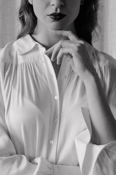 A black & white photo of a woman , from the waist to her chin. Her left hand is touching her chin