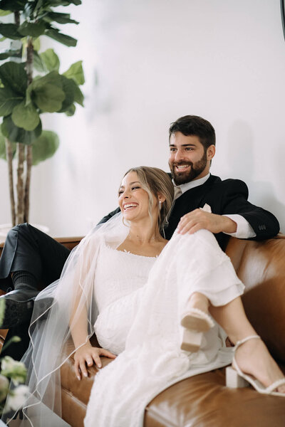 Bride lying on sofa with groom resting hand on her knee looking relaxed
