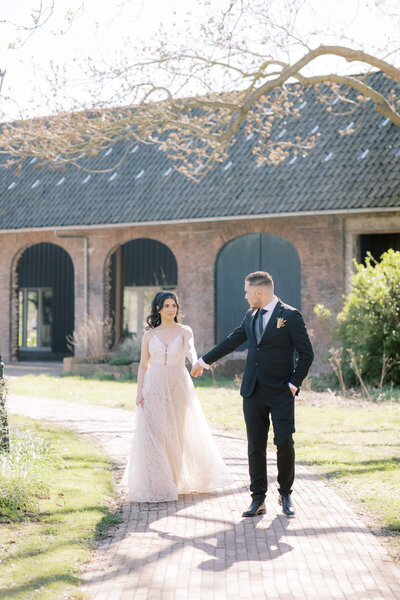 en elegant bruidspaar wandelt samen bij een landelijke locatie, met een authentieke trouwlocatie op achtergrond