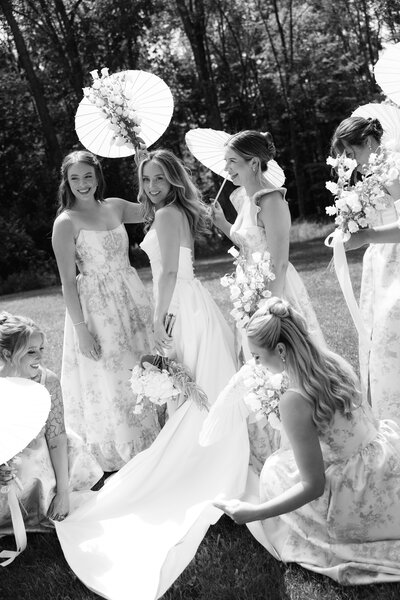 Black and white image of bride walking while bridesmaids hold her train