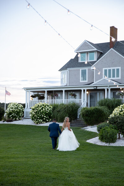 Rhode Island Wedding Photographer | Kelsey Sheehan Photography Timeless Rhode Island Weddings | A couple stands on a sandy beach at sunset, the woman in a white gown and the man in a dark suit. They lean in close, gazing at the serene ocean.