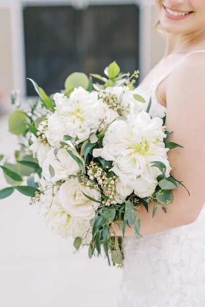 Close up of bride holding a big white bouquet with greenery