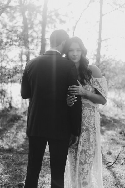a black and white photo of a bride and groom embrace during an intimate forest elopement in Spring, Texas. The bride gazes softly at the camera while holding the groom close, surrounded by natural light and trees.