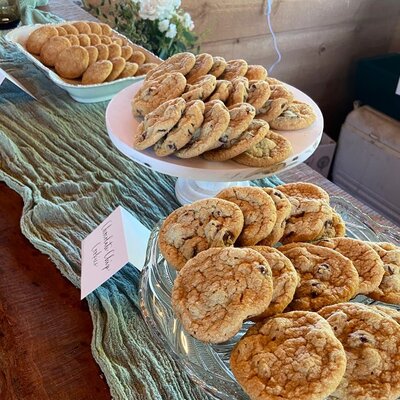Three plates of chocolate chip mini cookies are arranged in a line over a green cheesecloth decoration. 