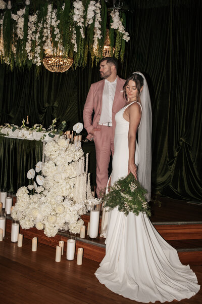 Newlywed couple standing beside an elegant floral arrangement featuring white flowers, glowing candles, and a sparkling crystal chandelier in a dimly lit, sophisticated indoor wedding venue near Portland, Oregon, captured by a Pacific Northwest wedding photographer.
