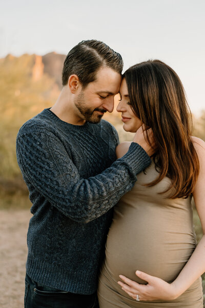 man holds woman while she holds pregnant belly