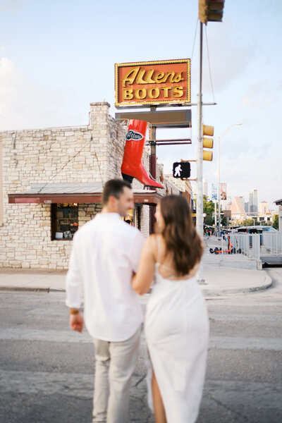Couple holding hands and walking with a boot store in the background