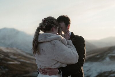 Couple share a kiss on a mountain during a snowy golden hour elopement in the Cairngorms, Scotland