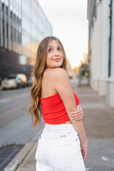 High school senior stands in front of her horse smiling and petting it.