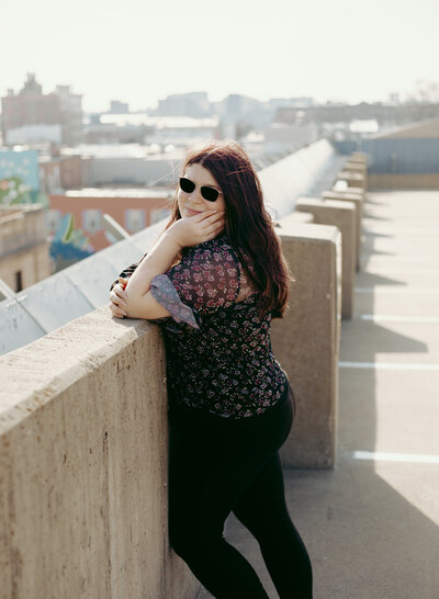 Joclyn leans up against the wall of a parking garage.