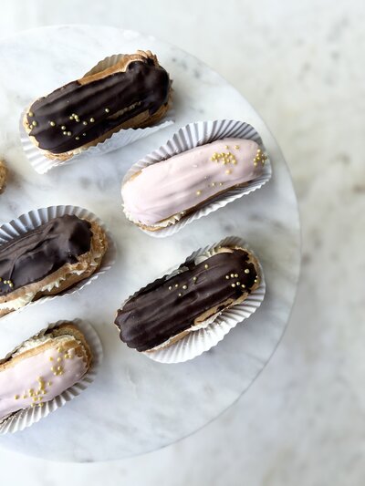 Chocolate dipped chantilly cream Eclairs on a white plate and marble table