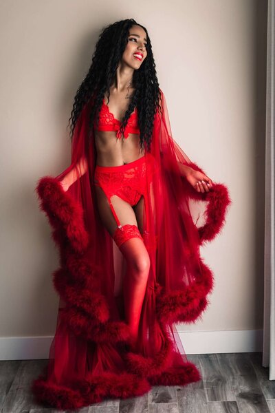 wearing a red gown and smiling a woman is posed during a boudoir photoshoot in Vancouver