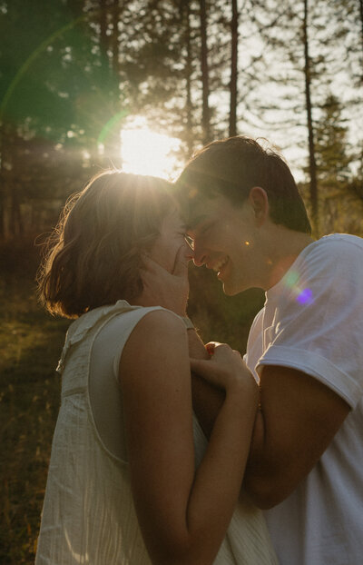 A man and woman are smiling at each other. Her arm is around his neck and his hand is around her waist.