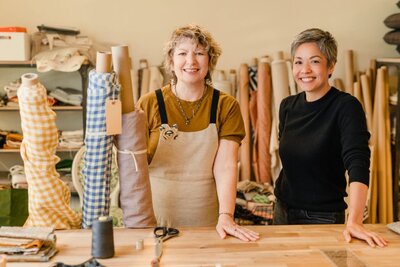 Two women business owners pose with bolts of fabric at their design studio