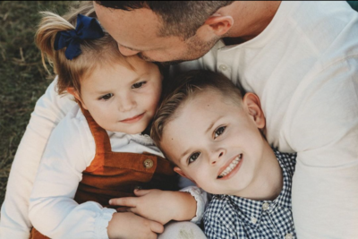Close up of dad kissing and hugging young daughter and son during family photography session.