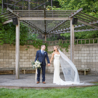 bride with flowing veil and groom  stands on platform together