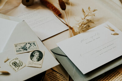White wedding invitations with sage green envelopes and historic blue and white stamps