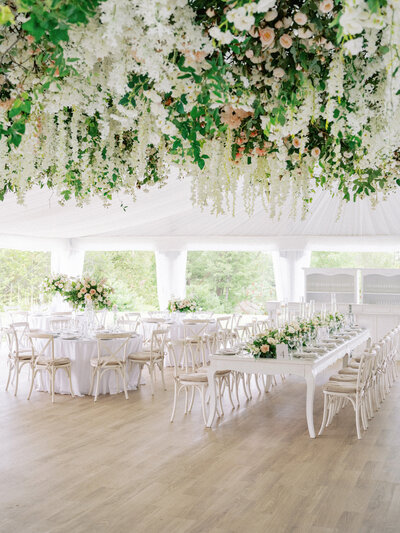 Wedding reception in a white tent with the ceiling covered in white and pink flowers and greenery