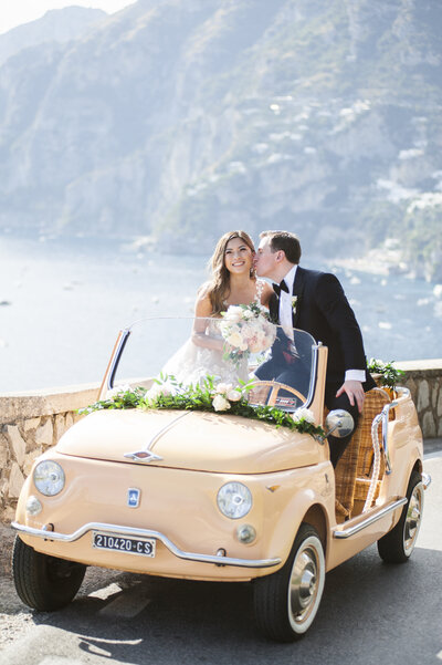 groom kisses bride sitting in Italian car