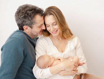 new parents holding baby girl in arms against a white backdrop at Heather Nicole Photography Studio.
