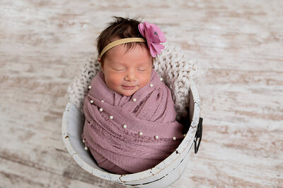 Newborn baby girl in pink wrapped snuggled in a white bucket