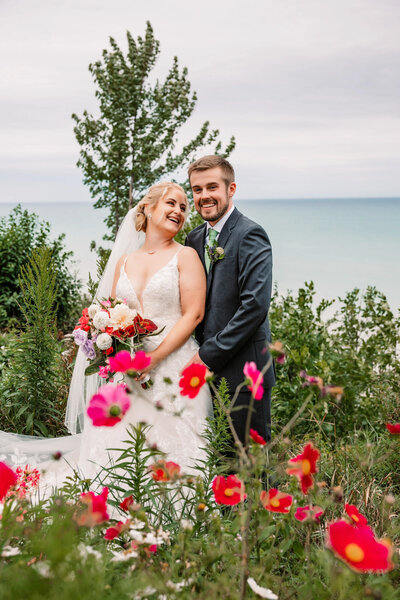 blonde bride and groom smile on the shores of lake michigan  in a private backyard wedding surrounded by gorgeous pink flowers