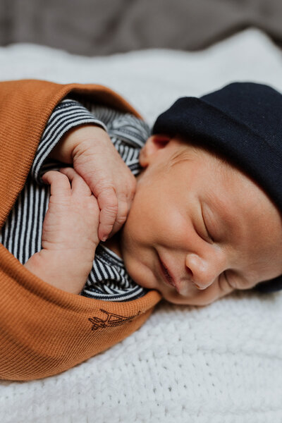 Newborn baby boy wrapped up and sleeping with a slight smile on his face.