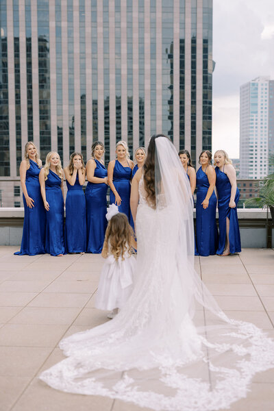 bride and flower girl standing in front of bridesmaids wearing blue dresses