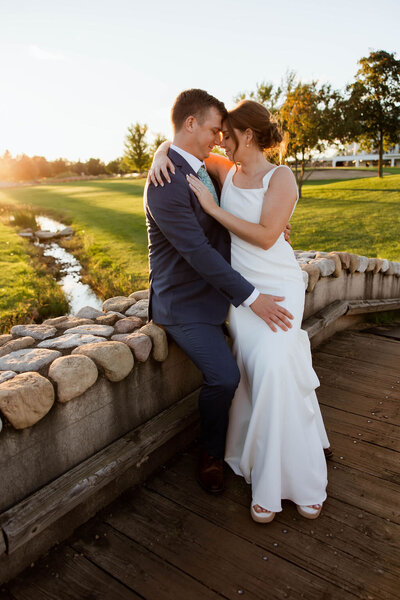 Wife sitting on her husband's lap on a stone wall in front of a creek in MN