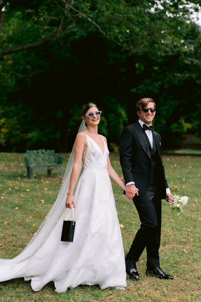 newlyweds in sunglasses walking on grass
