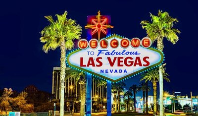 The famous "Welcome to Fabulous Las Vegas" sign, lit up at night and framed by tall palm trees against a deep blue sky. This iconic symbol captures the glamour and entertainment experiences offered through vacation fundraising for charities.